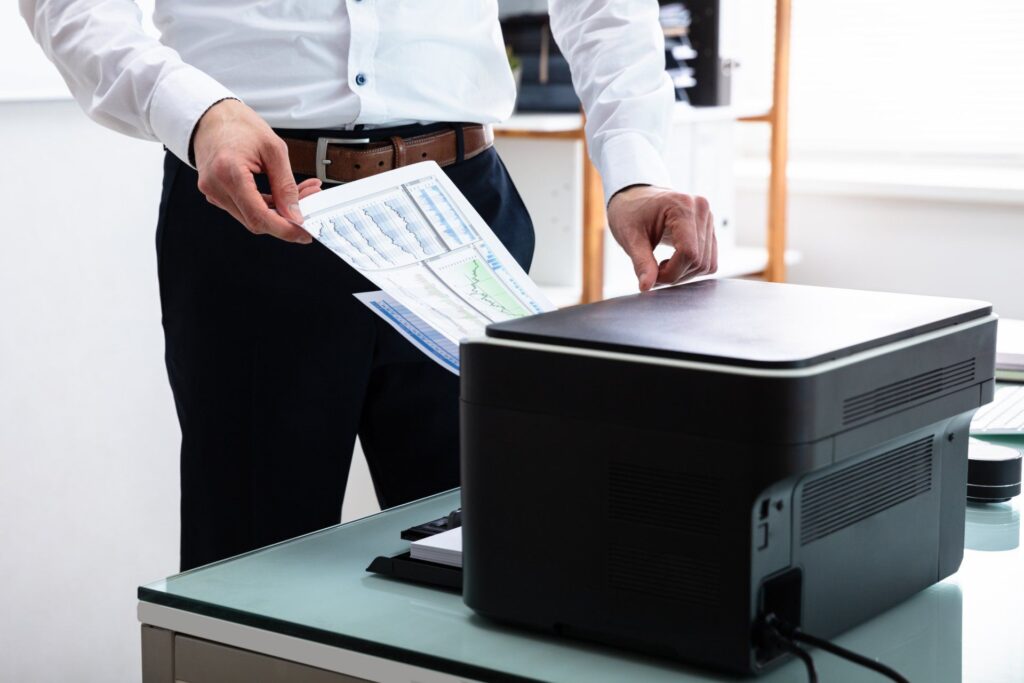A man is holding a piece of paper in front of a printer.