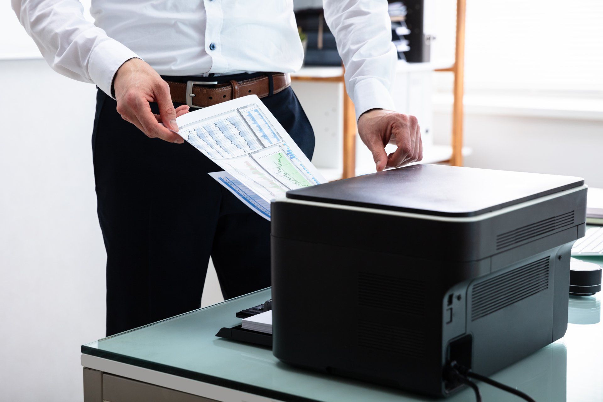 A man is holding a piece of paper in front of a printer.