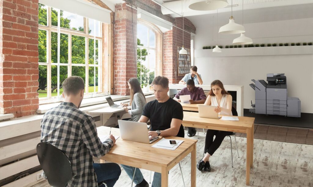 A group of people are sitting at tables in an office using laptops.