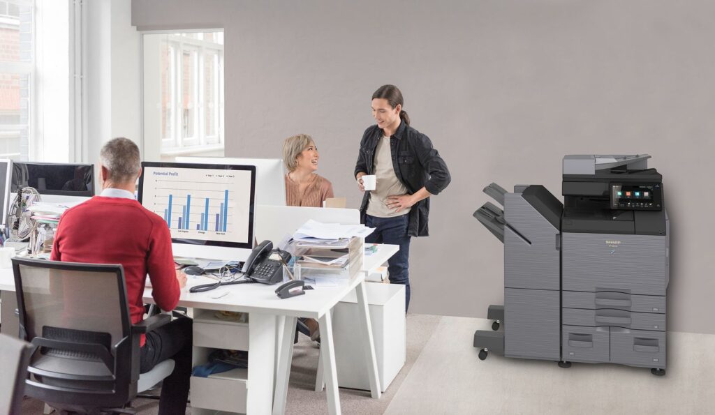 A man is sitting at a desk in an office next to a printer.