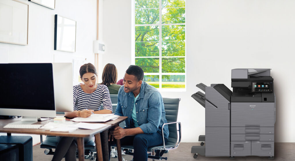 A man and a woman are sitting at a table in front of a printer.