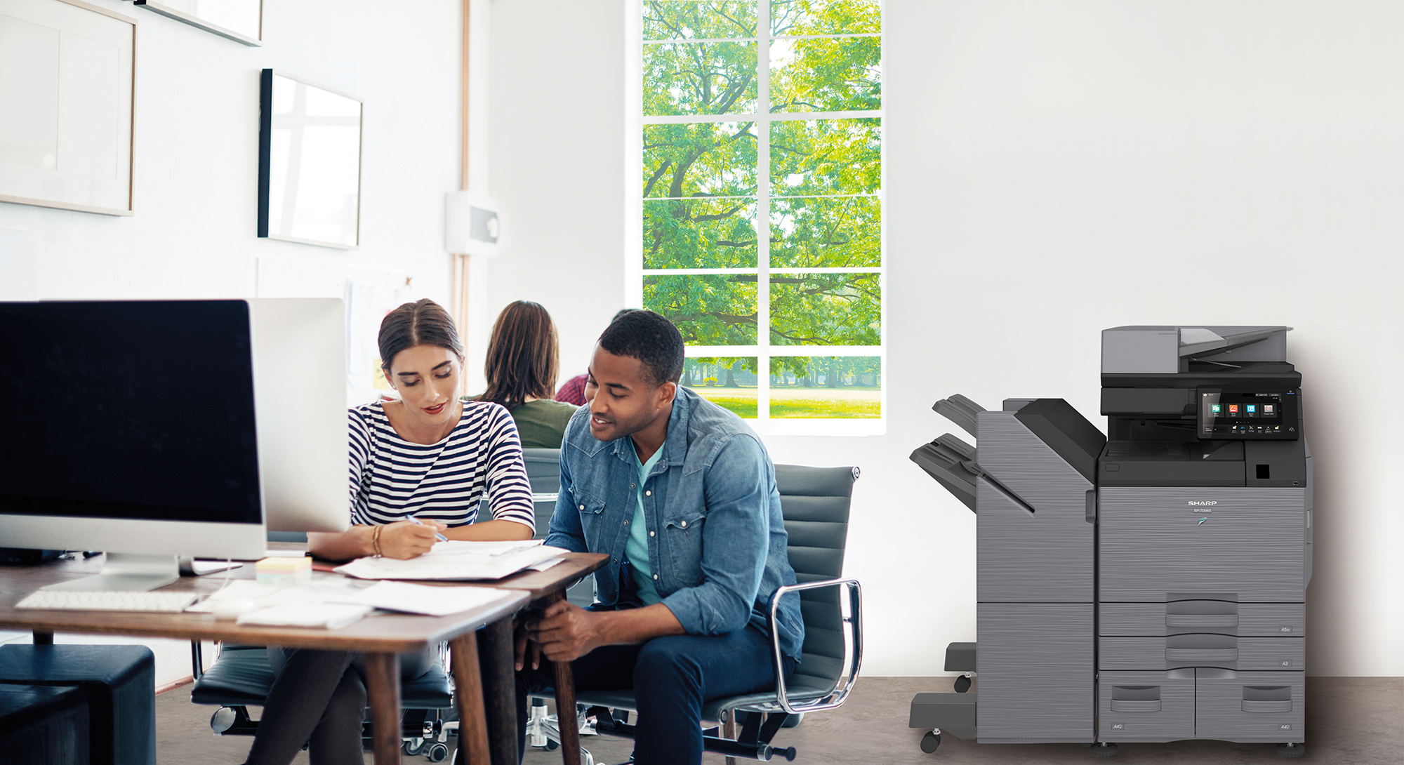 A man and a woman are sitting at a table in front of a printer.