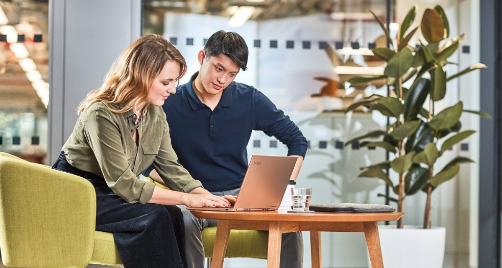 A man and a woman are sitting at a table looking at a laptop.