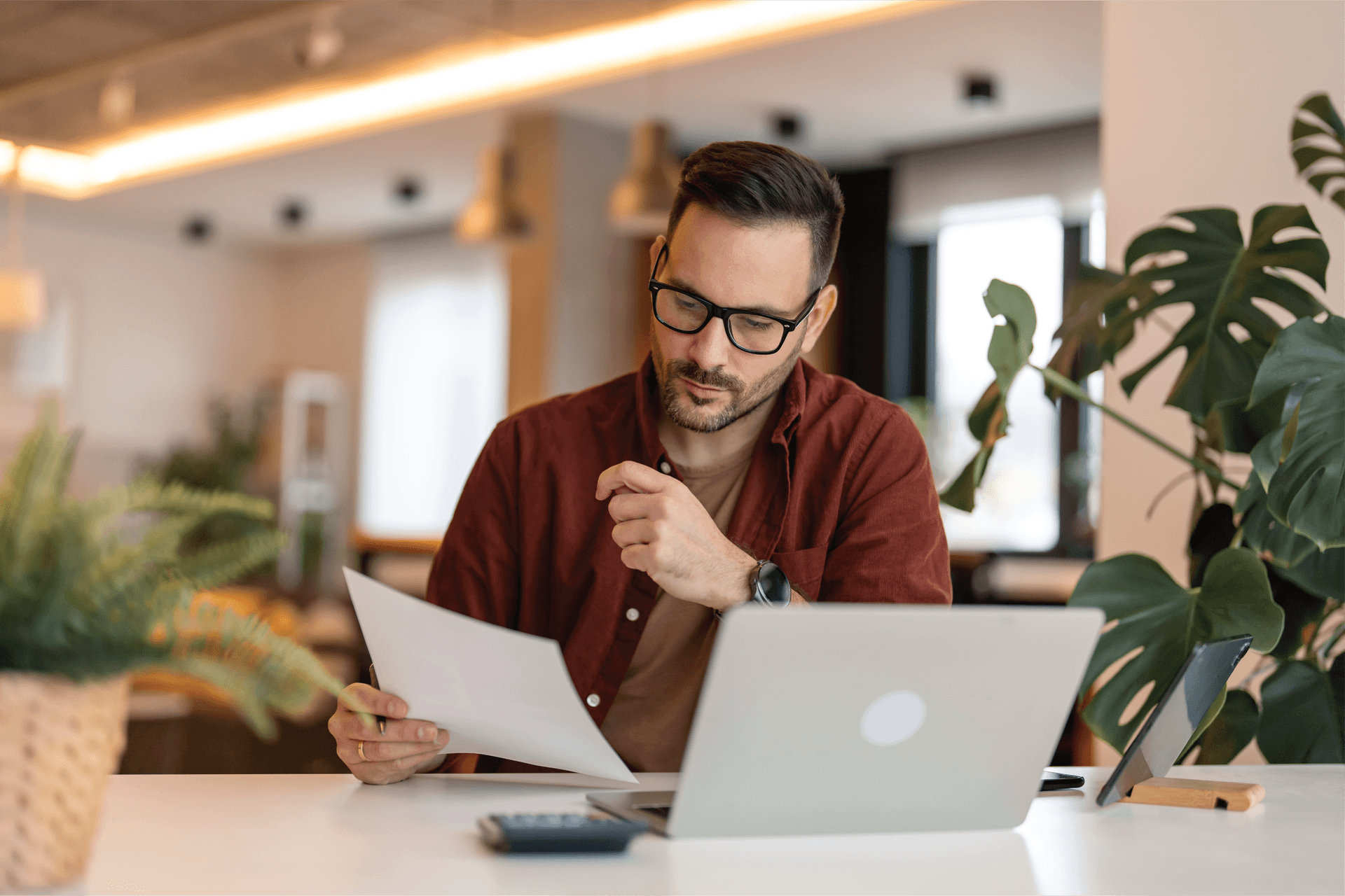 A man is sitting at a table with a laptop and a piece of paper.