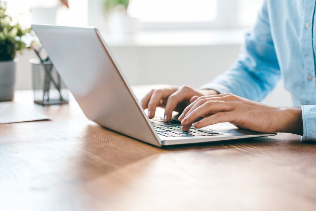 A person is typing on a laptop computer on a wooden desk.