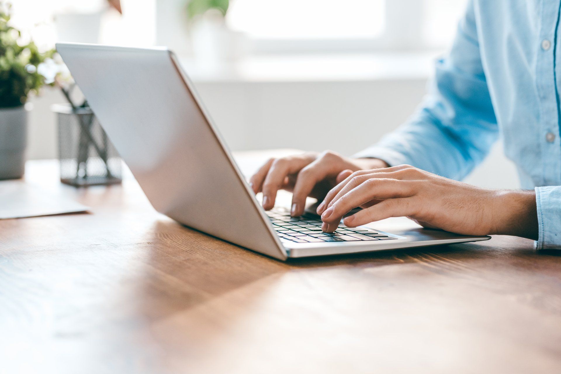 A person is typing on a laptop computer on a wooden desk.