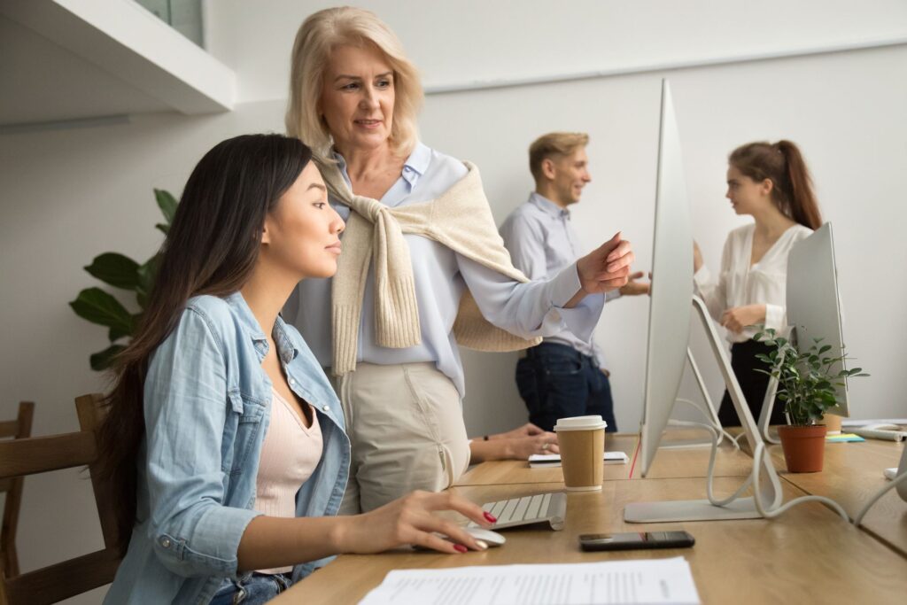 A woman is teaching a young woman how to use a computer in an office.