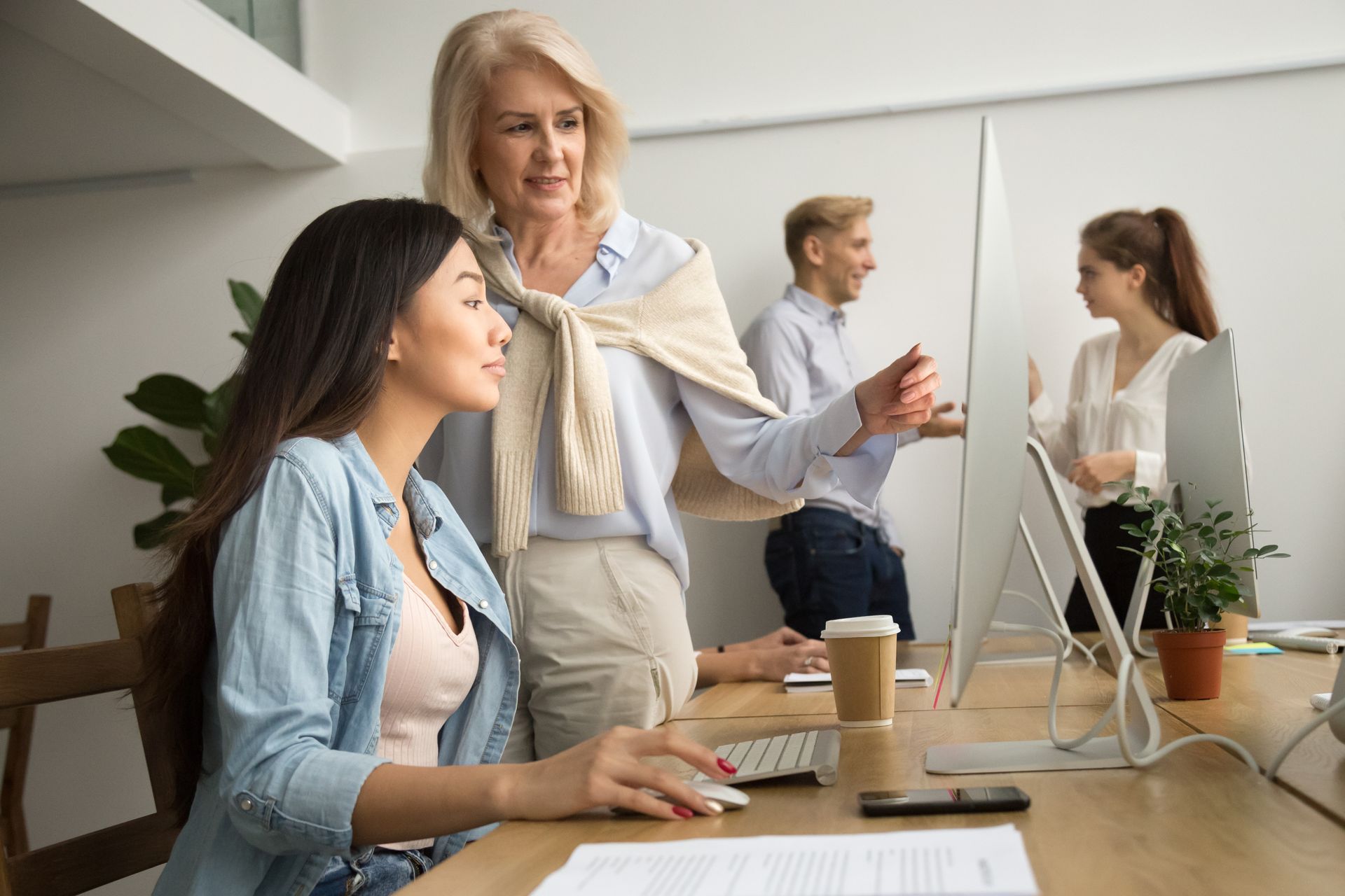 A woman is teaching a young woman how to use a computer in an office.