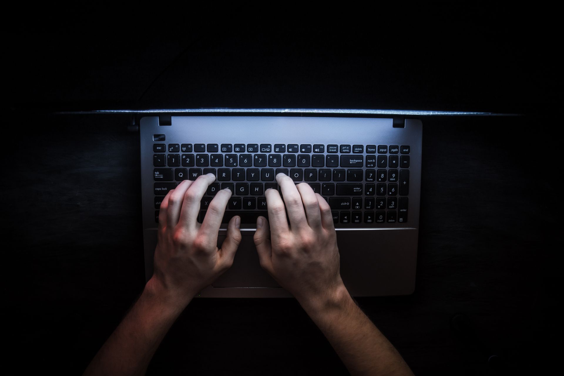 A person is typing on a laptop computer in the dark.