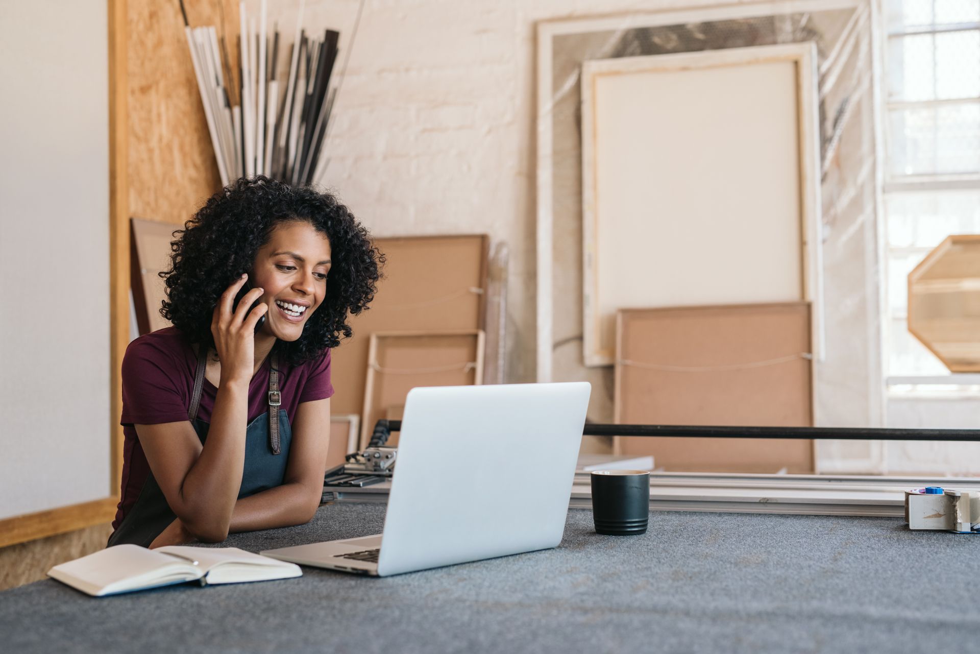 A woman is sitting at a table with a laptop and talking on a cell phone.