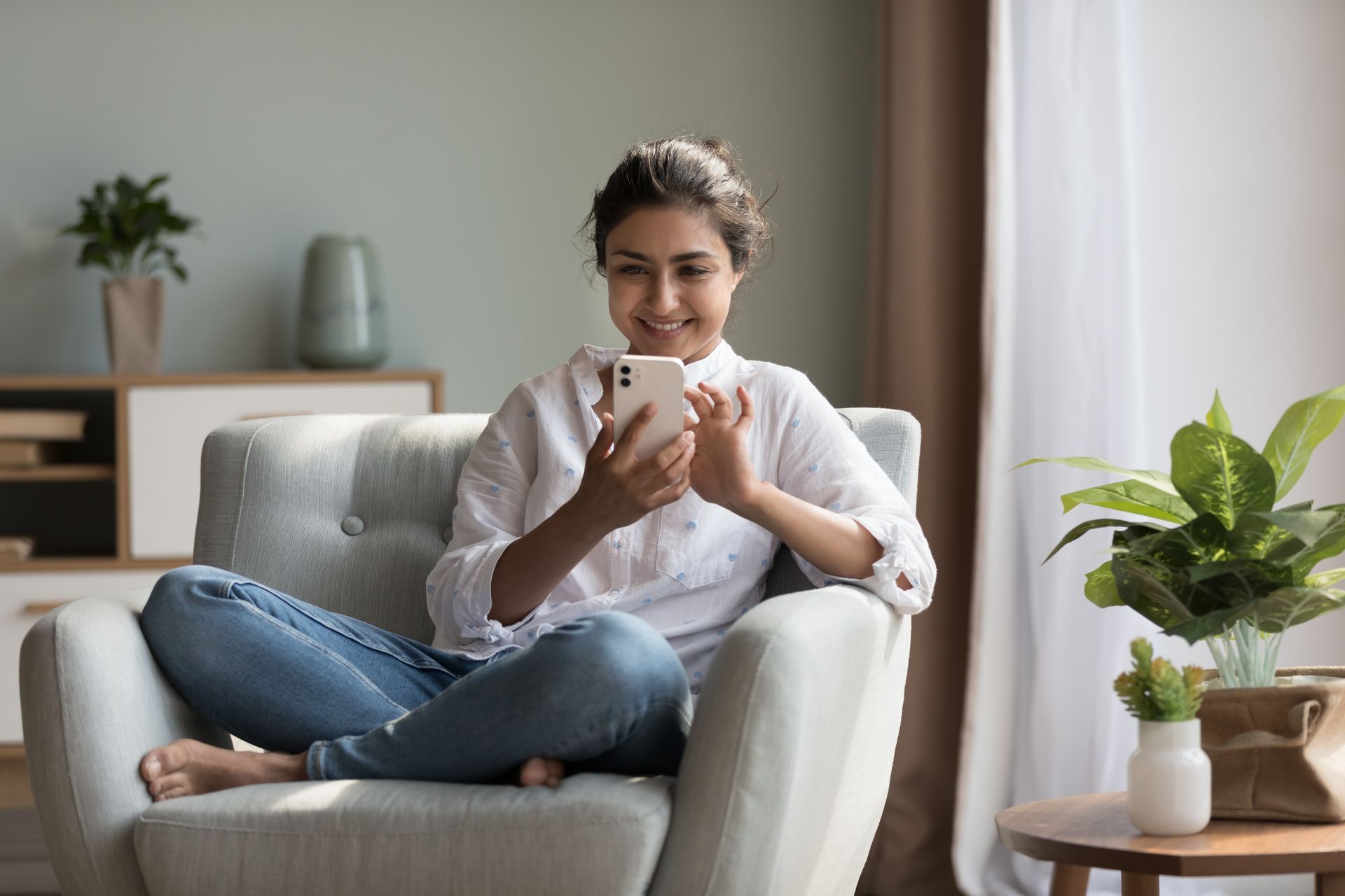 A woman is sitting in a chair looking at her cell phone.