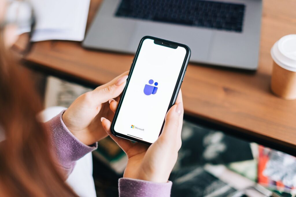 A woman is holding a cell phone with the teams app on it.