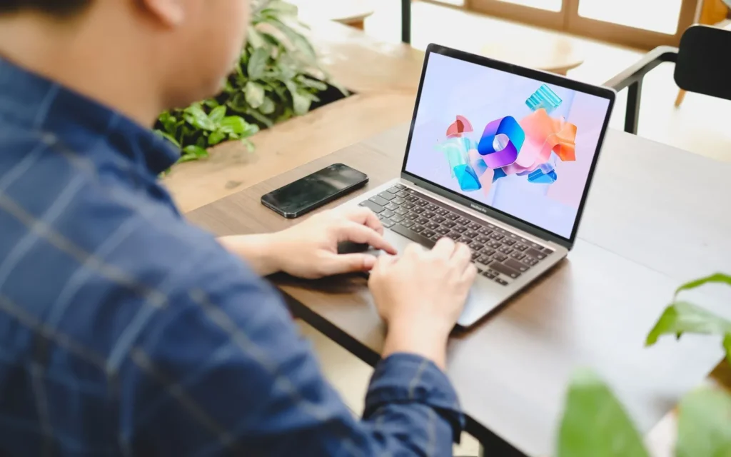 Person working on a laptop showing the Microsoft 365 logo at a shared workspace