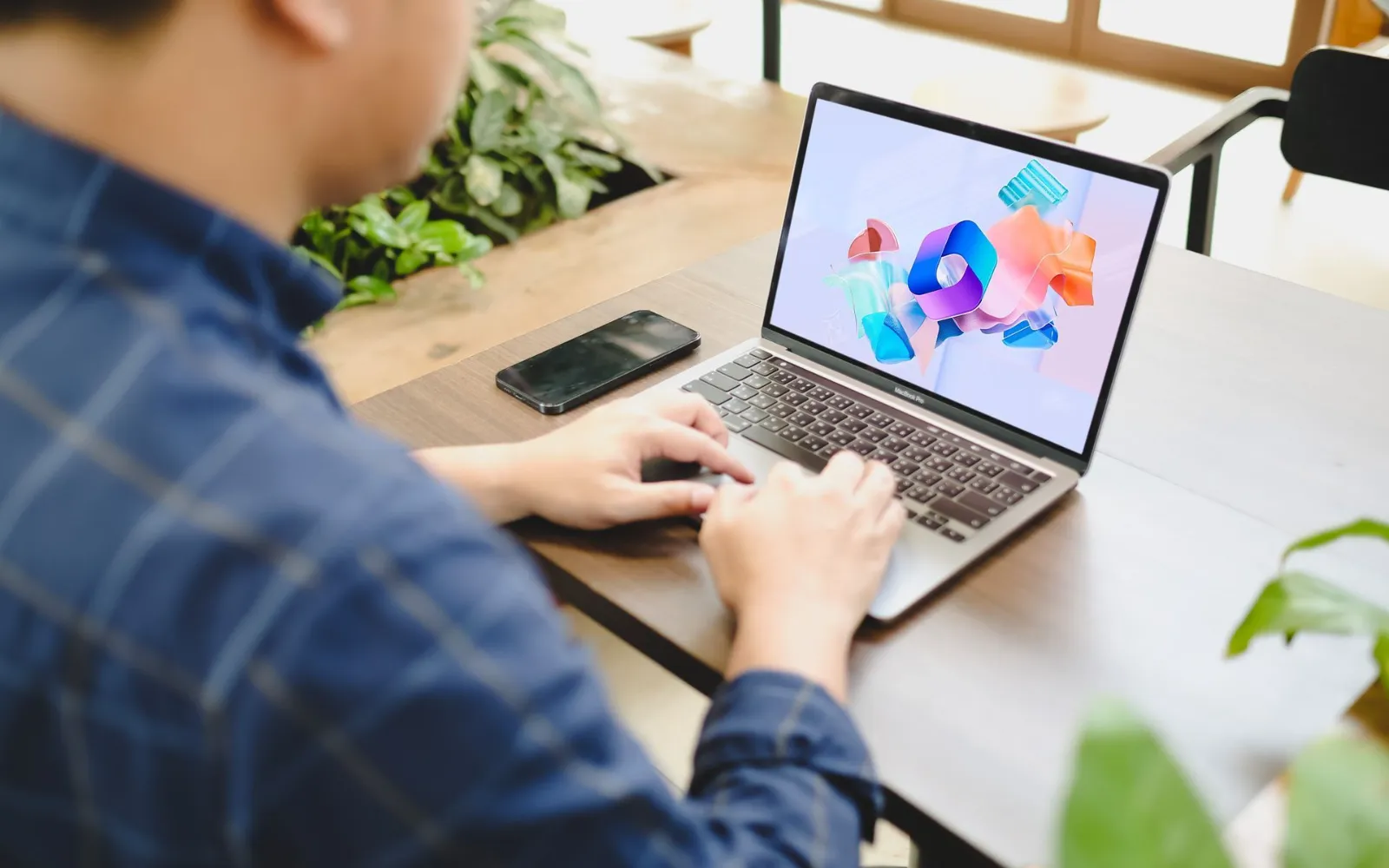 Person working on a laptop showing the Microsoft 365 logo at a shared workspace